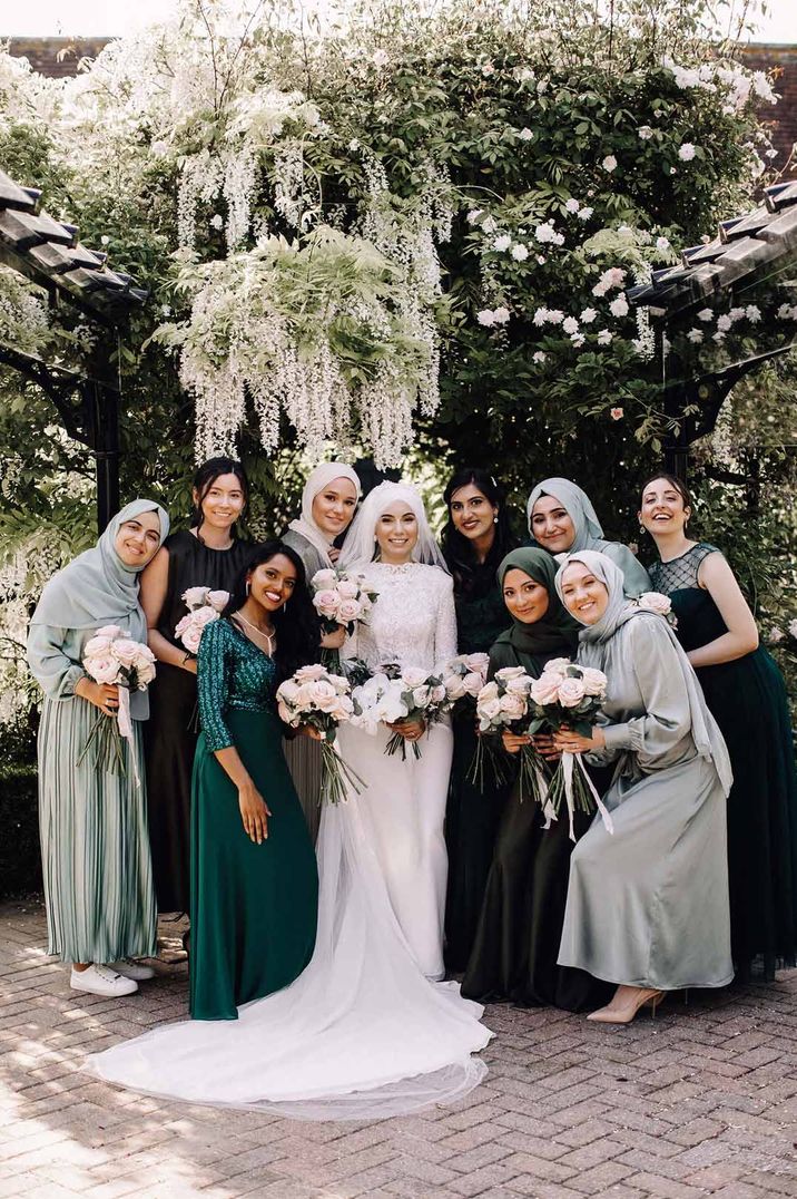 Bride in long sleeve lace wedding dress standing with bridesmaids in mismatched sage green, forest green and black bridesmaid outfits 