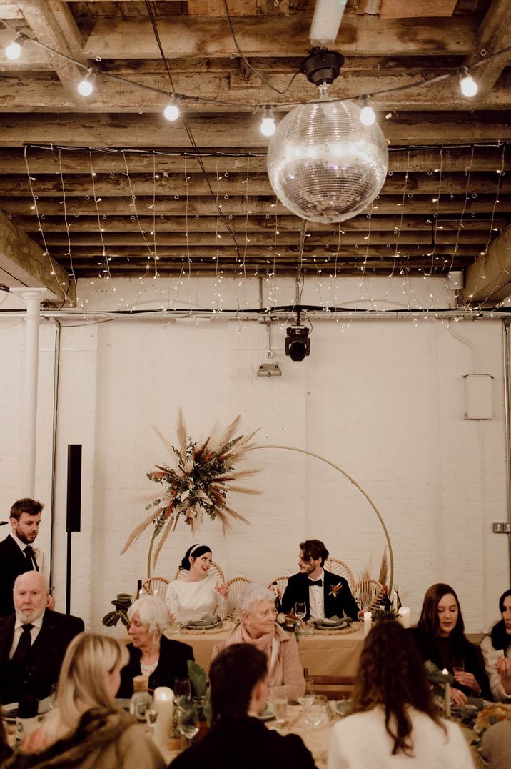 The newlyweds sit for their wedding breakfast at industrial style wedding venue with modern table arrangements 