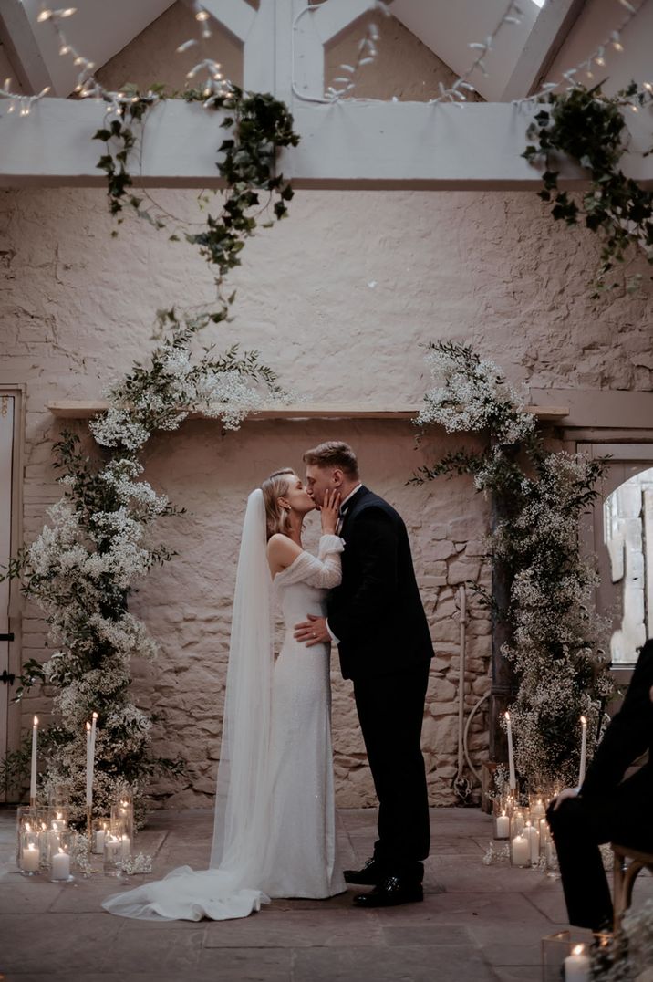 The bride and groom share their first kiss as a married couple at their winter wedding with white floral decorations 