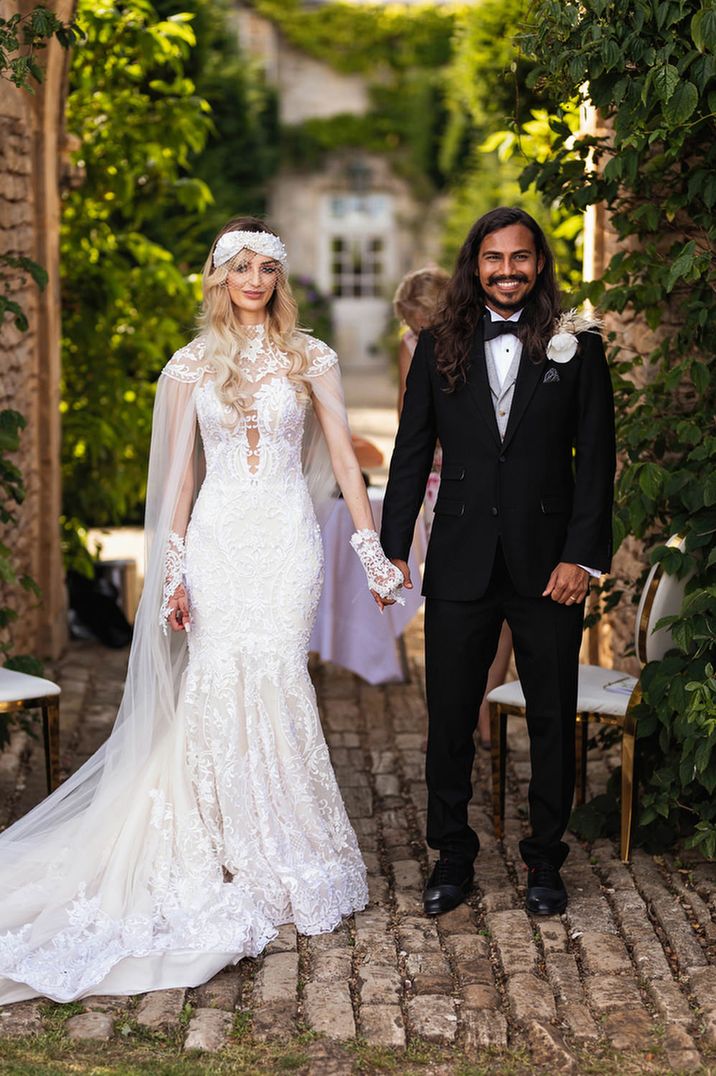 Stylish bride in a lace Wona Concept wedding dress and Indian groom in a black tuxedo