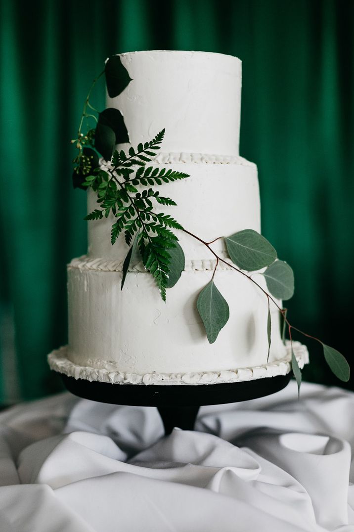 Three-tiered white wedding cake with green foliage embellishments 