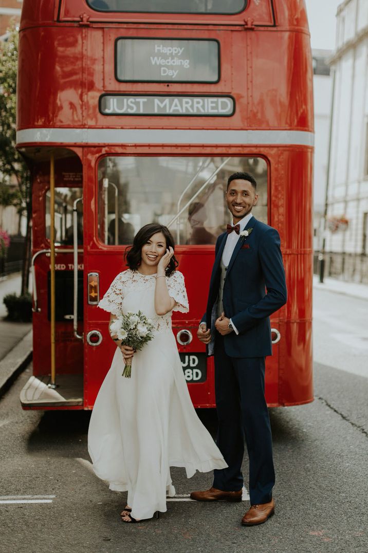 Classic red London wedding bus with "just married" sign, short sleeve wedding dress and dark blue suit 