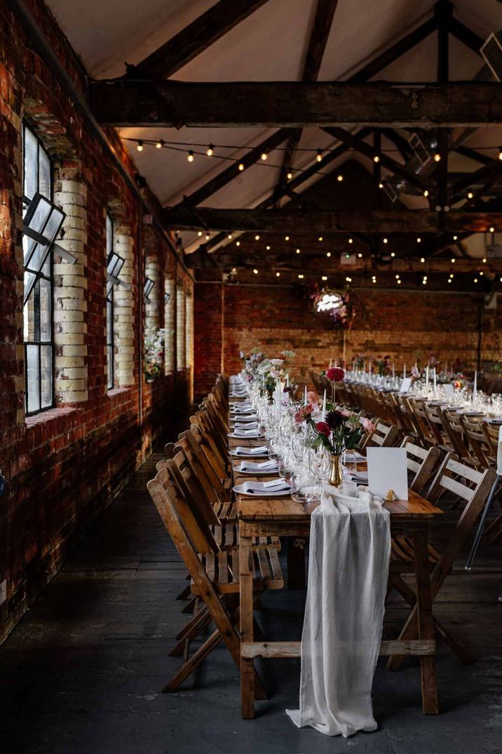 Rustic neutral wedding tablescape at Loft Studios London - white sheer table runners, fairy lights in the beams, and red rose floral centrepieces 