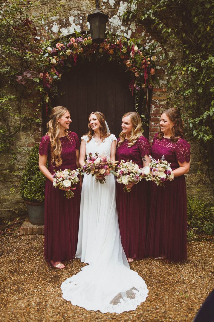 Bridesmaids in burgundy lace bridesmaid dresses with bride in lace wedding dress at Ramster Hall 