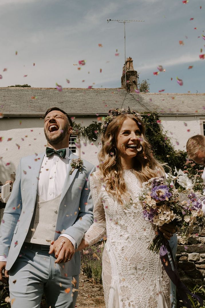 Bride in long sleeve high neck boho lace wedding dress having confetti exit with groom in pale baby blue three piece suit 