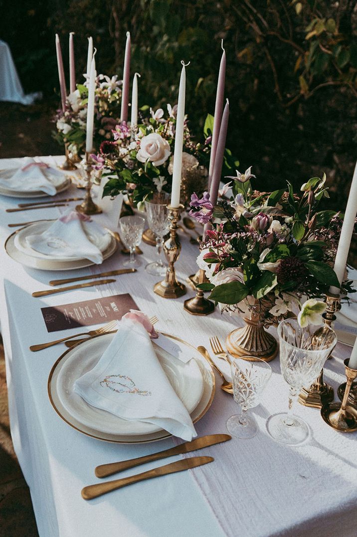 Purple and white taper candles with gold rimmed plates, gold cutlery, and crystal glassware 