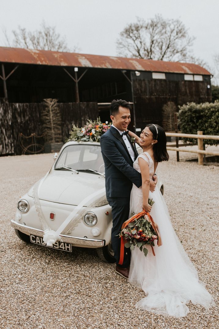 Couple standing in front of white Fiat 500 wedding cars with lace decorations