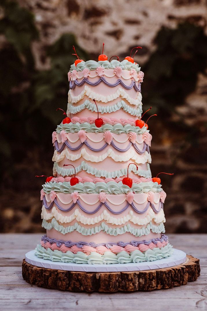 Three tier retro wedding cake with pink, purple, white and mint green icing and lots of cherries