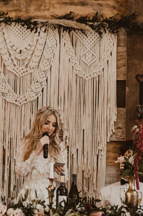 Bride in custom-made lace detail dress giving speech in front of large boho macrame display