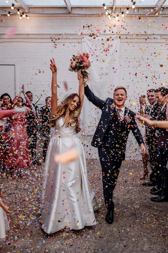 Bride and groom have bright and colourful confetti exit from their industrial style wedding 