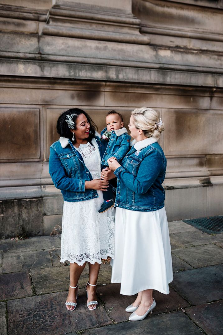 Two brides wearing dark blue denim jackets with white fur trim collars matching their little boy 