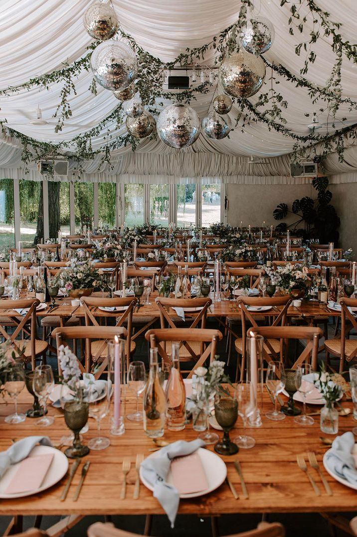 Marquee wedding breakfast at Ridge Farm decorated with disco balls and foliage with pink taper candles on the tables 