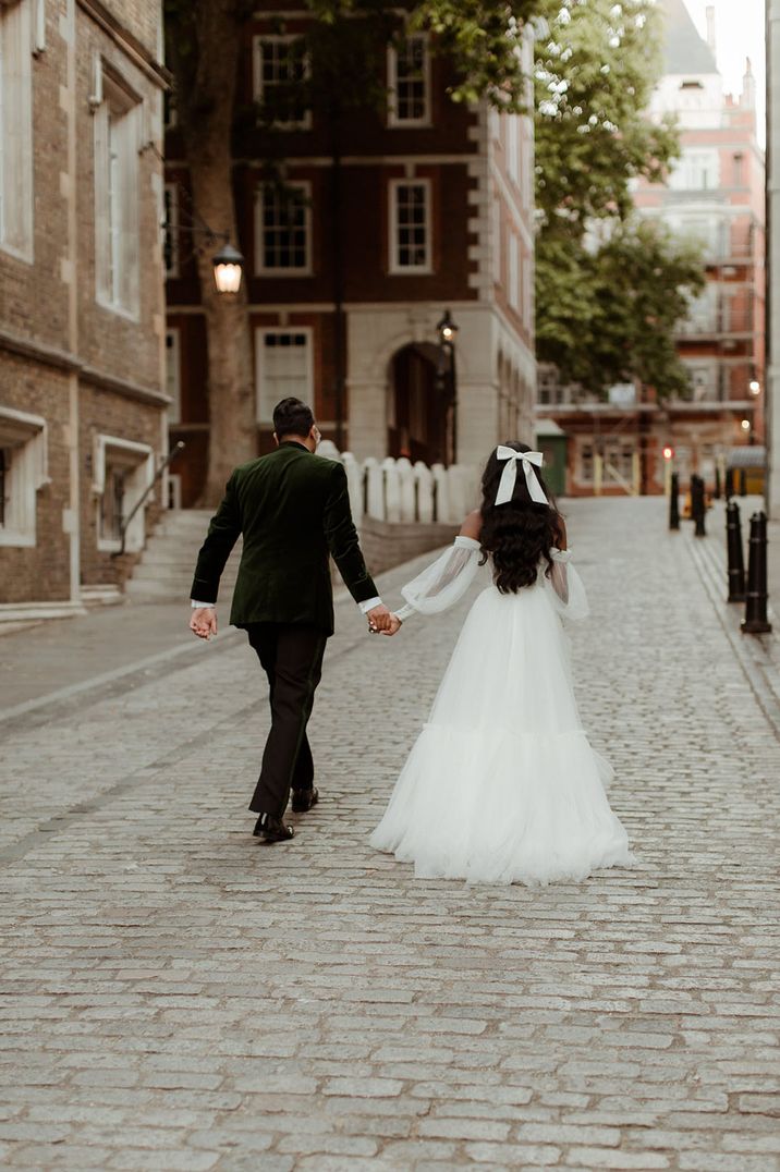 City wedding with the bride in a white wedding gown with white hair bow accessory walking hand in hand with the groom in a green velvet suit jacket