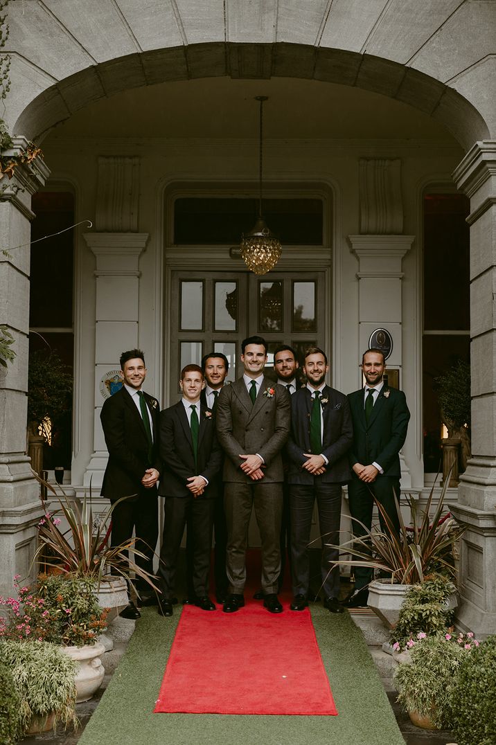 The groom and groomsmen all wear dark wedding suits posing together 