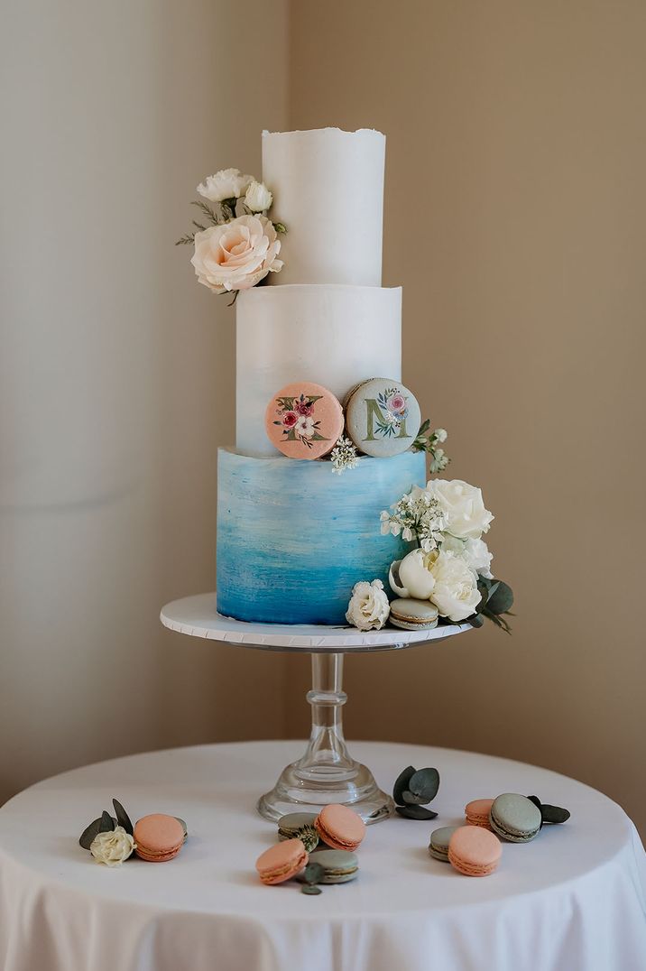 Three tier blue ombre iced wedding cake with pastel macaroons and white roses 