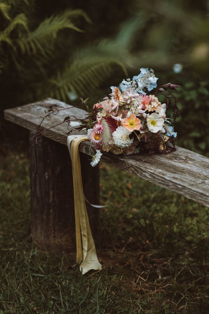 Colourful wildflower wedding bouquet tied with ribbon resting on a wooden bench 