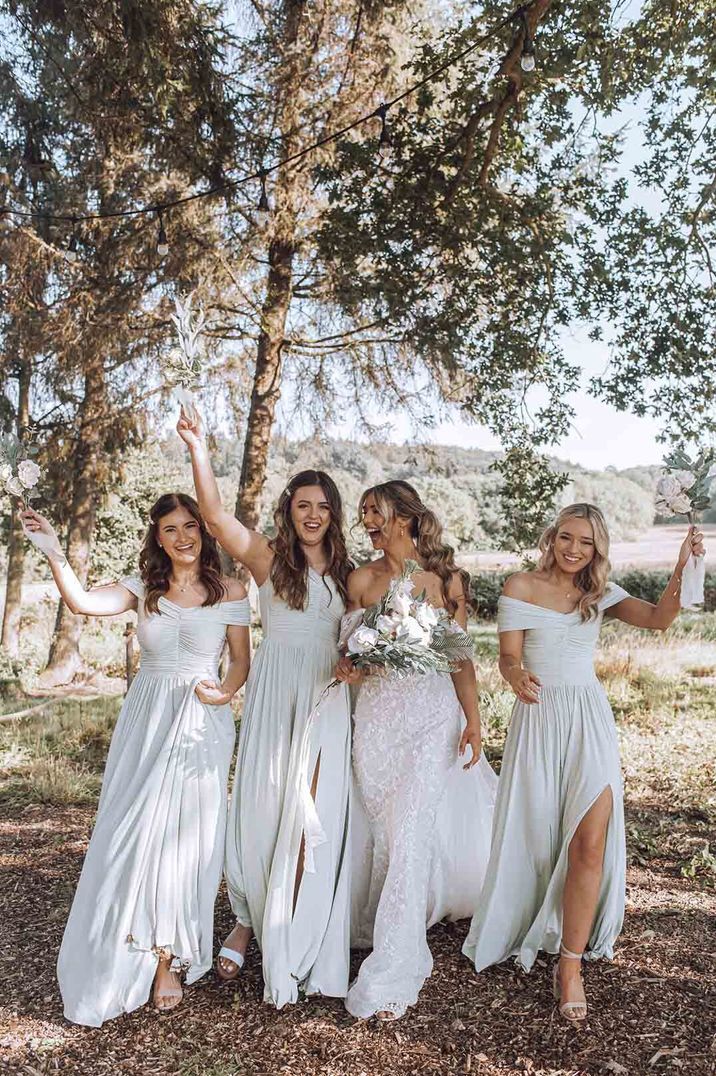 Bridal party wearing satin-look off shoulder bridesmaid dresses and white embellished wedding dress standing amidst the trees at Oak Tree Barn 