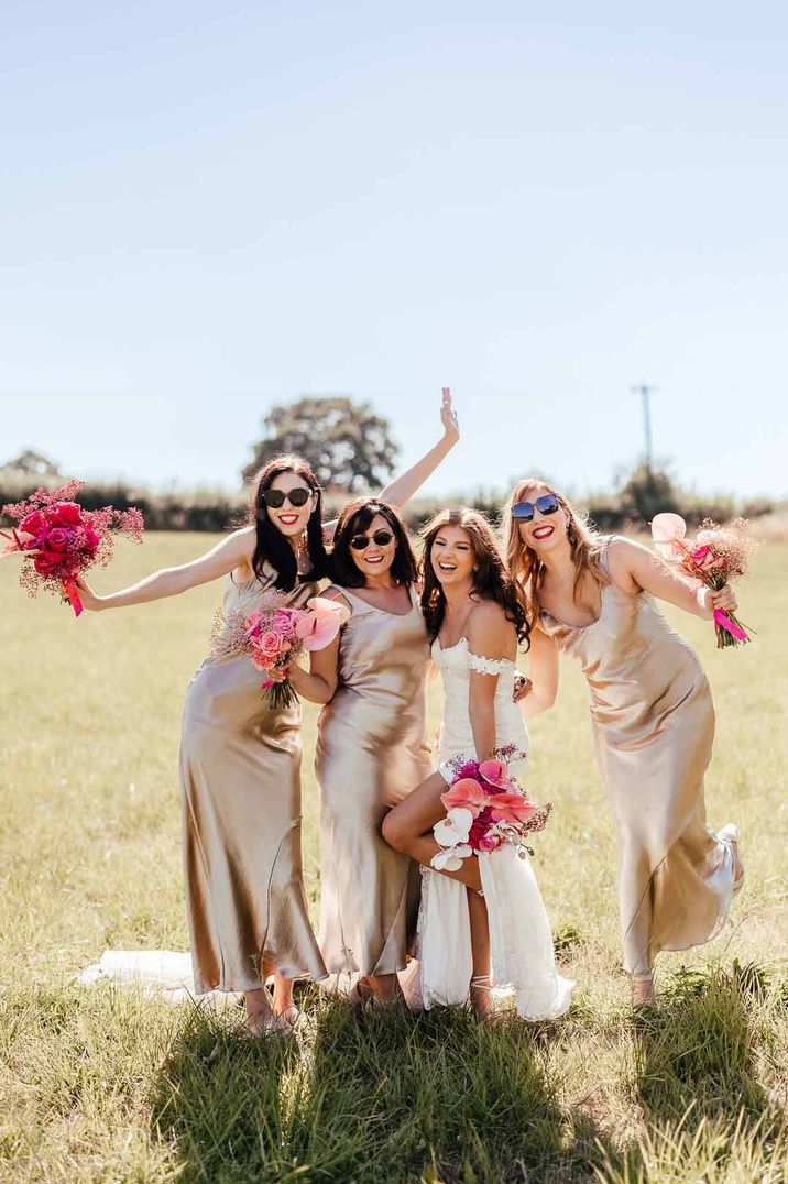 Bride in off the shoulder lace wedding dress standing with bridesmaids in gold satin slip bridesmaid dresses - hen party ideas