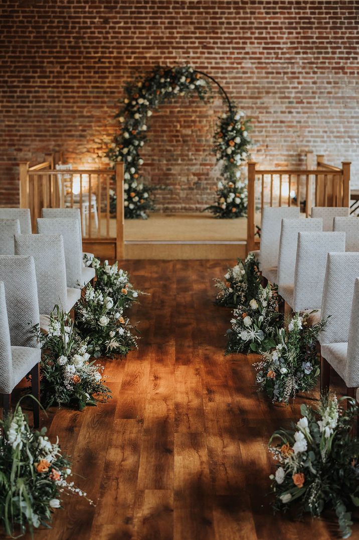 Cooling Castle Barn wedding venue decorated with orange and white wedding flower aisle arrangements and floral arch decor 