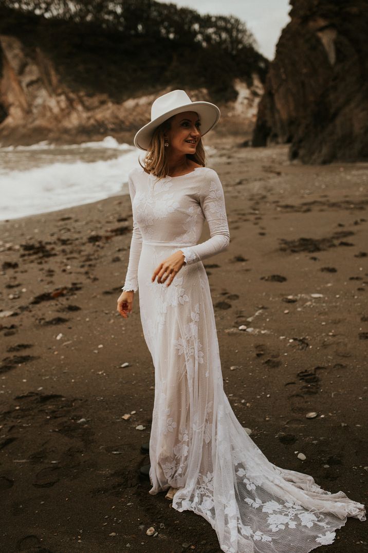 Bride in a lace long sleeve wedding dress and fedora hat for beach wedding