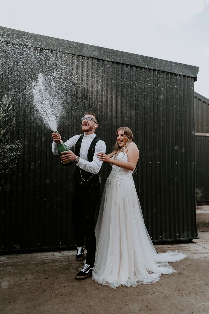 Bride in white strapless dress and groom doing champagne pop