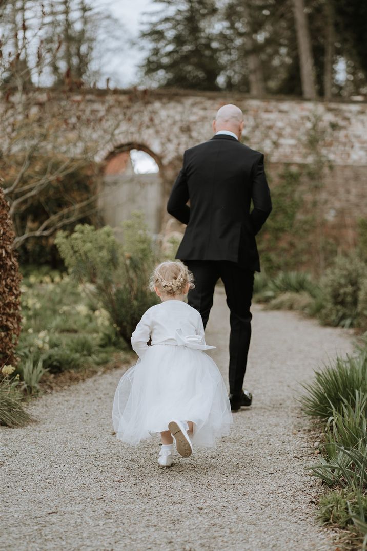 Young flower girl in white cardigan running after the groom 