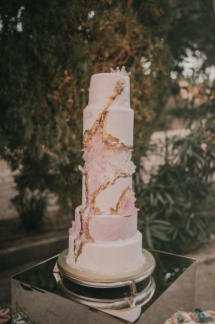 Luxury tall wedding cake with white icing and crystal pink geode style with gold detailing 