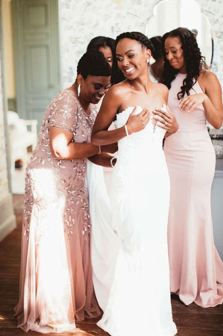 Bride in strapless deep v neck wedding dress getting help from her bridal party in pink mismatched bridesmaid dresses 