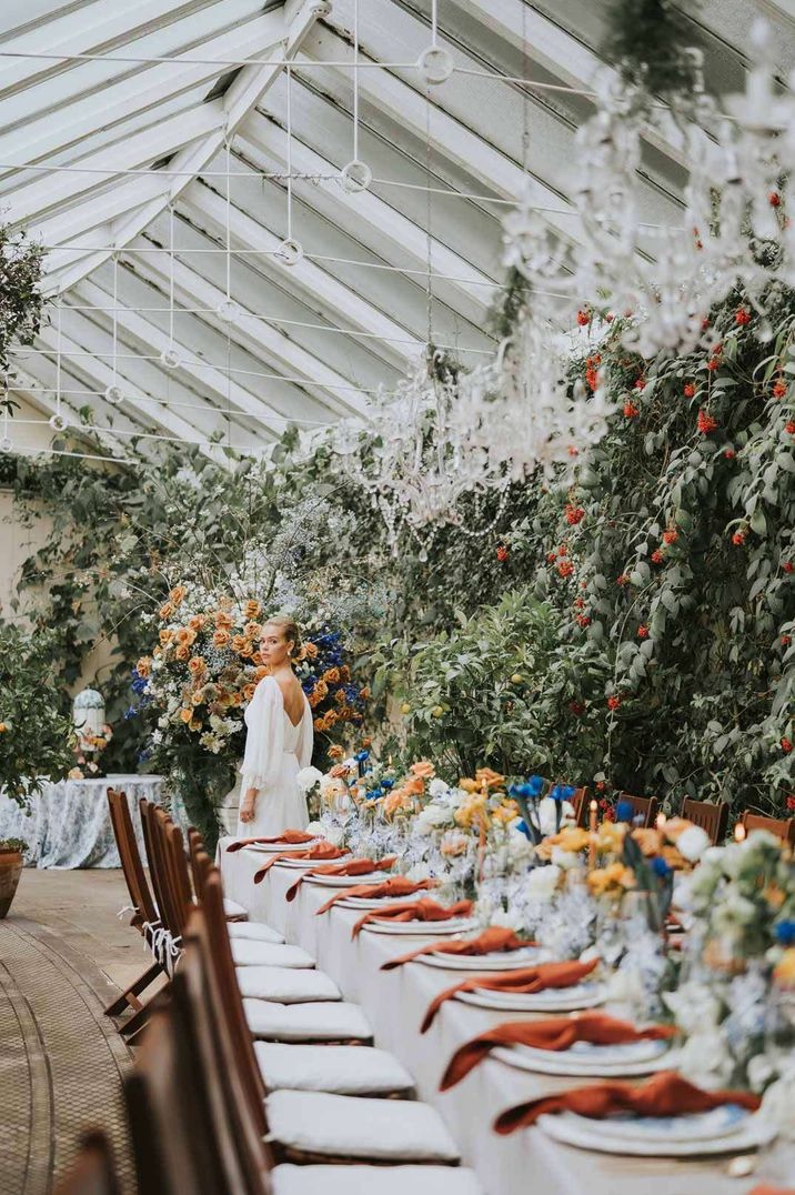 Bride in long sleeve wedding dress by classic wedding tablescape with white tablecloth and burnt orange napkins at Sezincote House