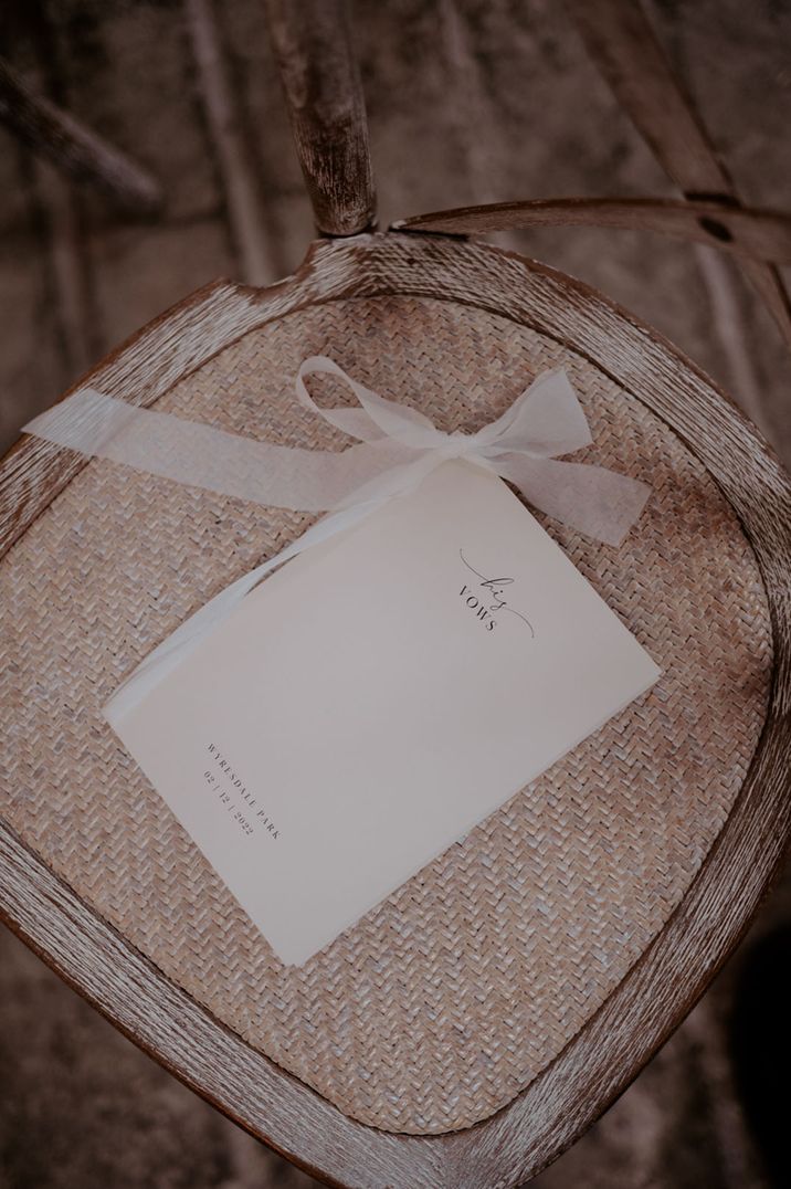 Wedding vow booklet tied with pink ribbon resting on a rattan chair 