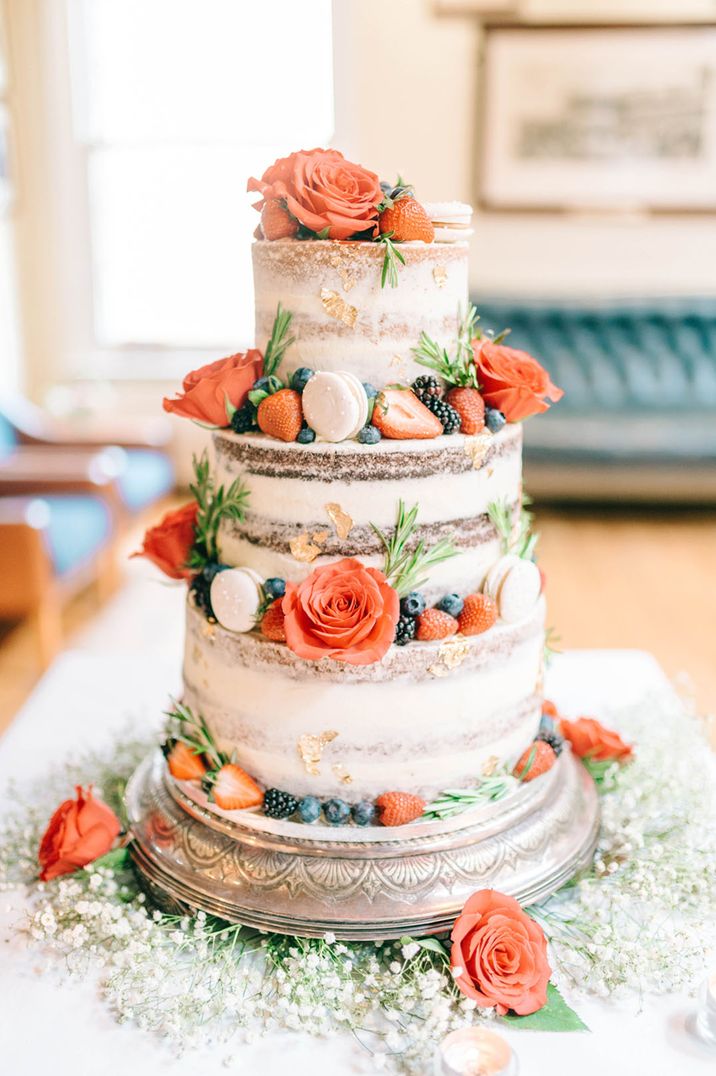 Three tier semi naked wedding cake decorated with gold flakes, red roses, white macaroons and more 