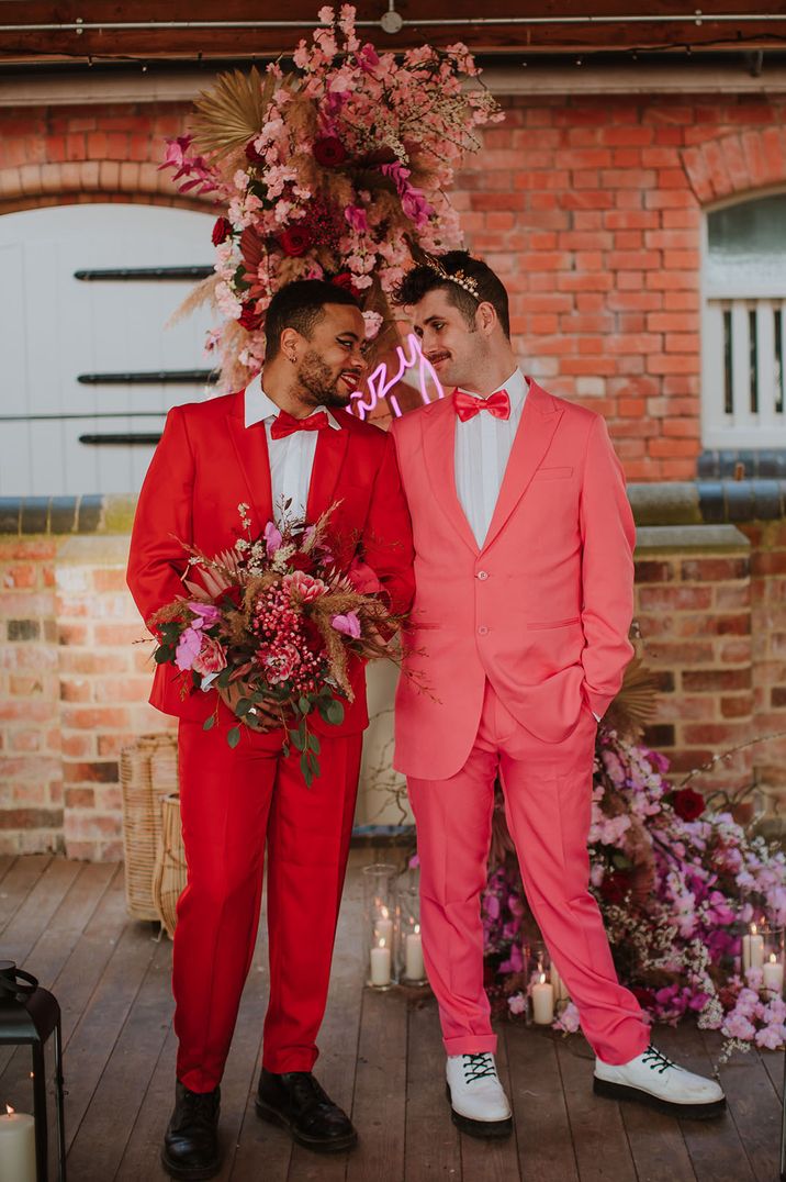 Two grooms wearing a red and pink wedding suit with matching bow ties and accessories for Valentine's Day inspired wedding 