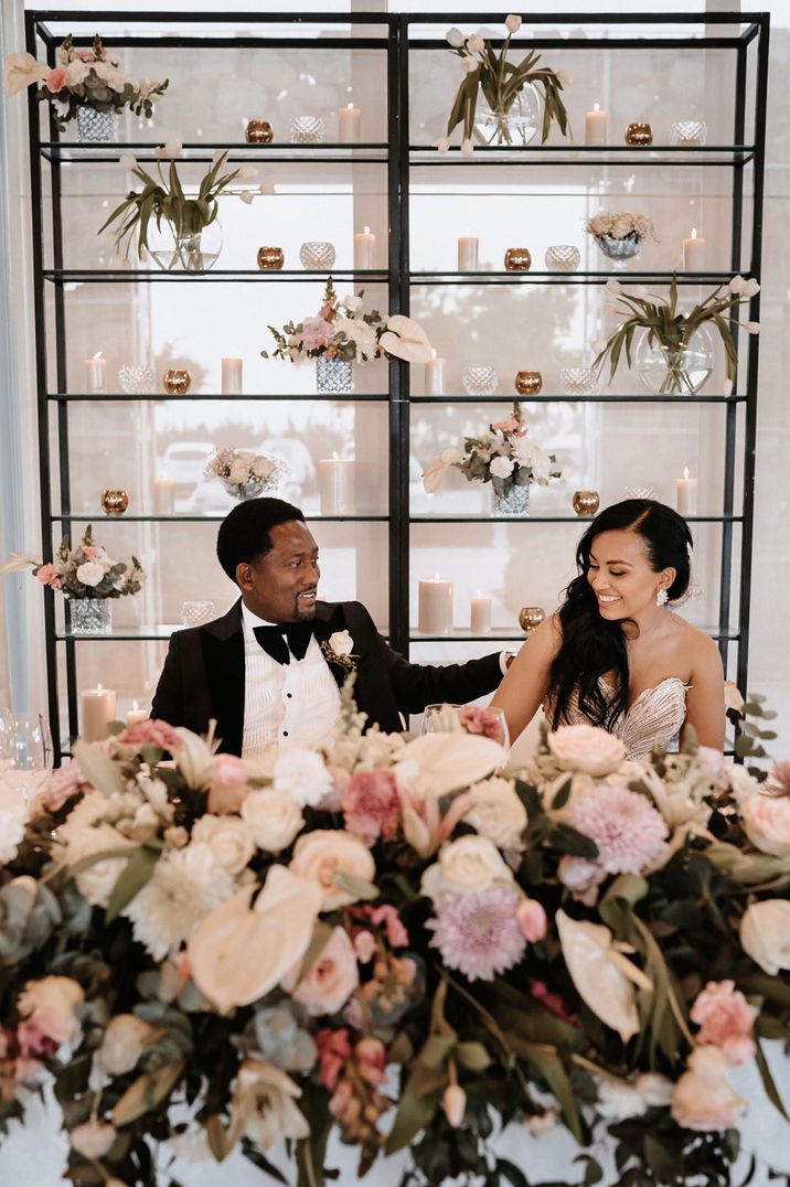 Bride and groom sitting at their sweetheart table with blush pink and white flower arrangement including anthuriums 