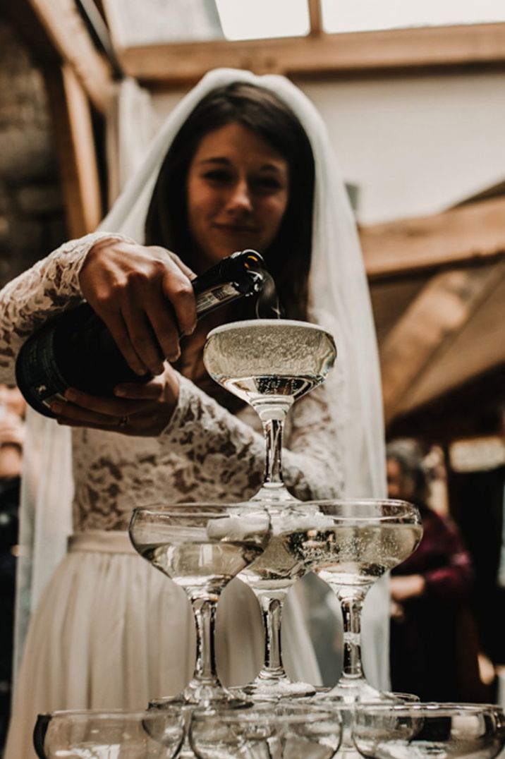 Bride in long sleeve lace wedding dress pouring champagne into the champagne tower 