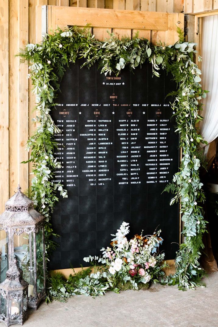 Large black and white peg board wedding table plan with foliage and flowers