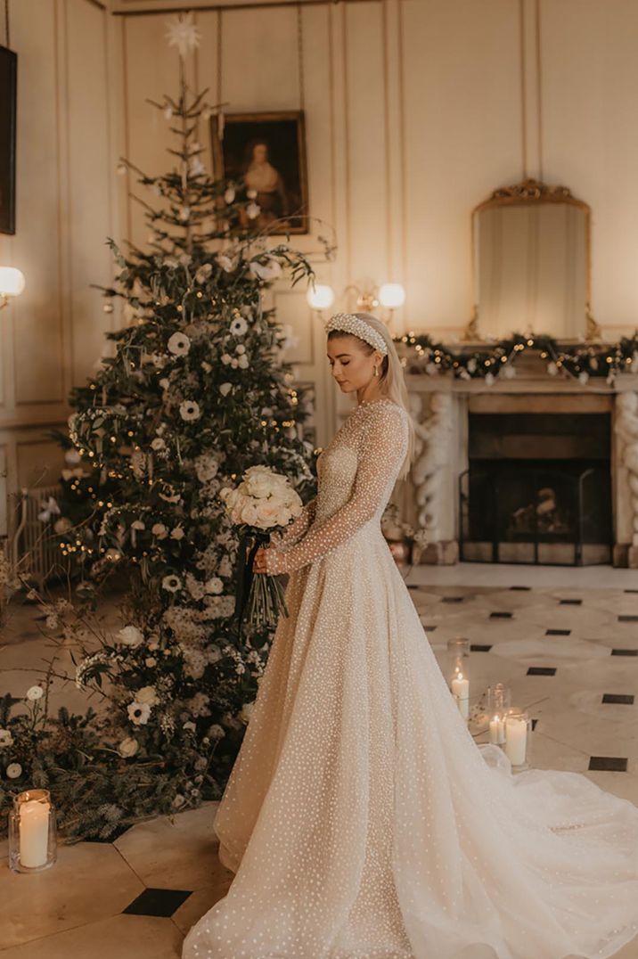 Bride in a sparkly wedding dress stands in front of a Christmas tree 