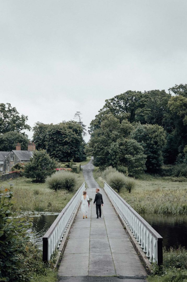 Bride and groom walking over the bridge on the grounds of Crom Castle glasshouse wedding venue Northern Ireland 