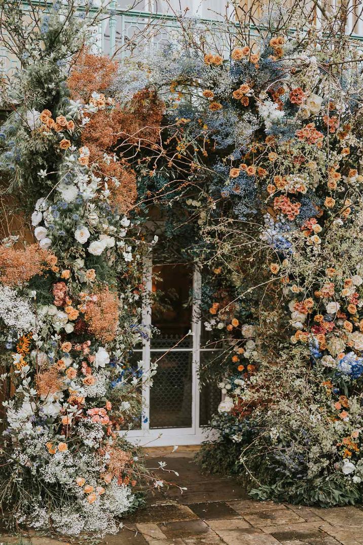 Large colourful flower arch with white garden roses, orange dried flowers, blue baby's-breath, eucalyptus, orange peonies and more 