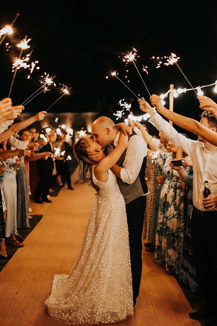 Bride in pearl embellished princess wedding dress kissing groom during wedding sparkler exit 