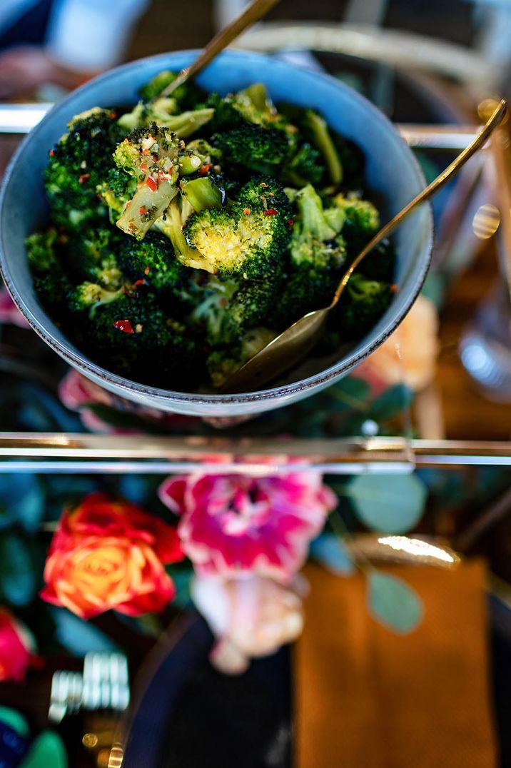 Chilli and garlic broccoli in blue bowl with gold serving tool for wedding breakfast 