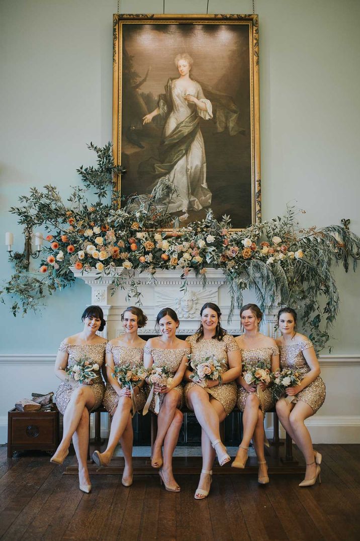 Bridal party sat on chair at Oxfordshire wedding venue wearing short off the shoulder gold bridesmaid dresses 