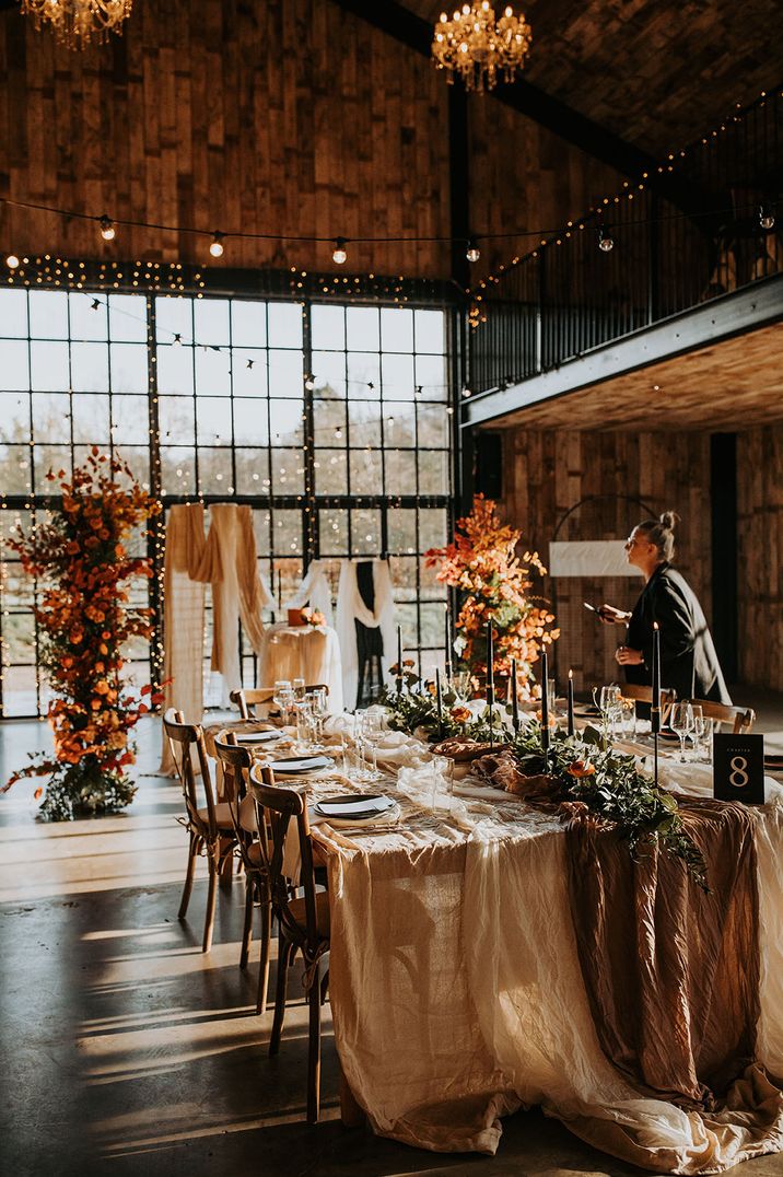 Autumnal theme wedding with a burnt orange colour scheme, soft white drapery and black taper candles 