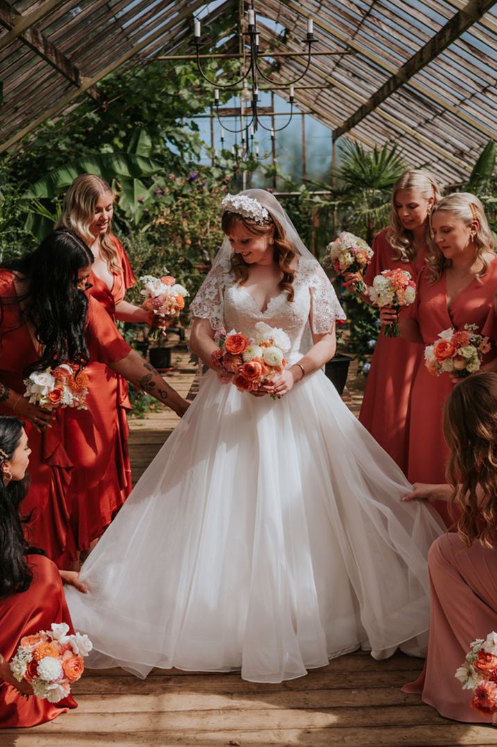 Bridal party in coral bridesmaid dresses with the bride in glasshouse wedding venue 