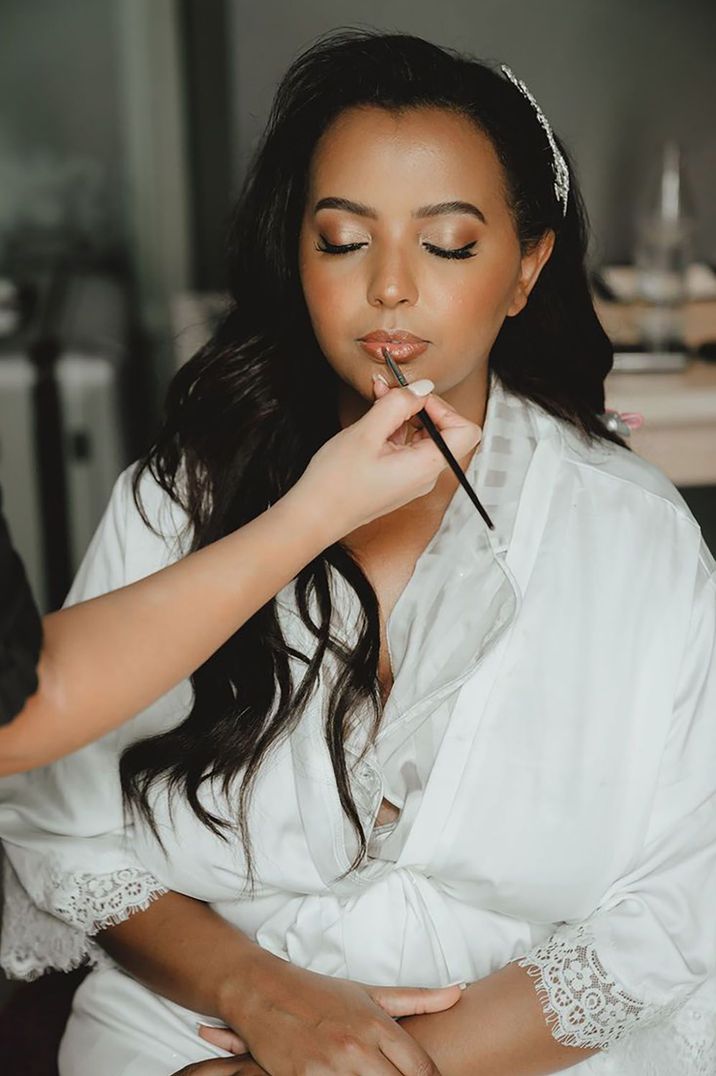 Bride in white robe getting her makeup done for destination wedding in Thailand with side swept hair 