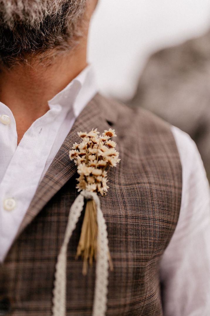 Groom in a beige check waistcoat with a dried flower and lace ribbon buttonhole