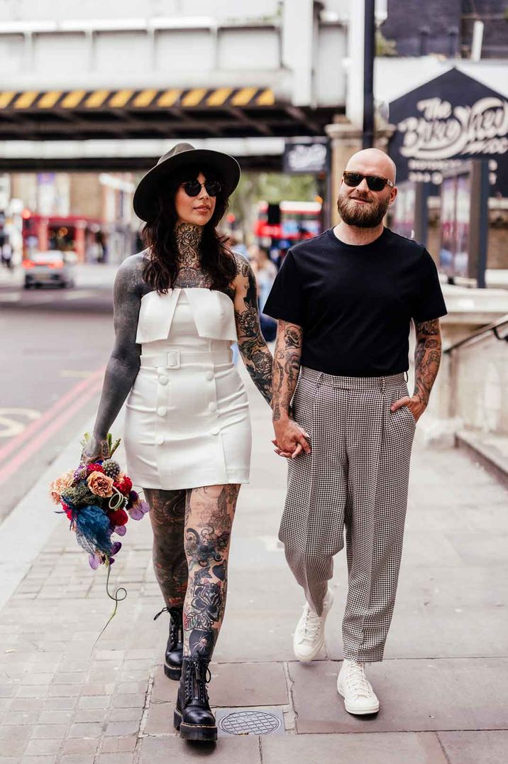 Alternative wedding - bride in strapless short wedding dress with buttons and belt standing with groom in casual grooms wear