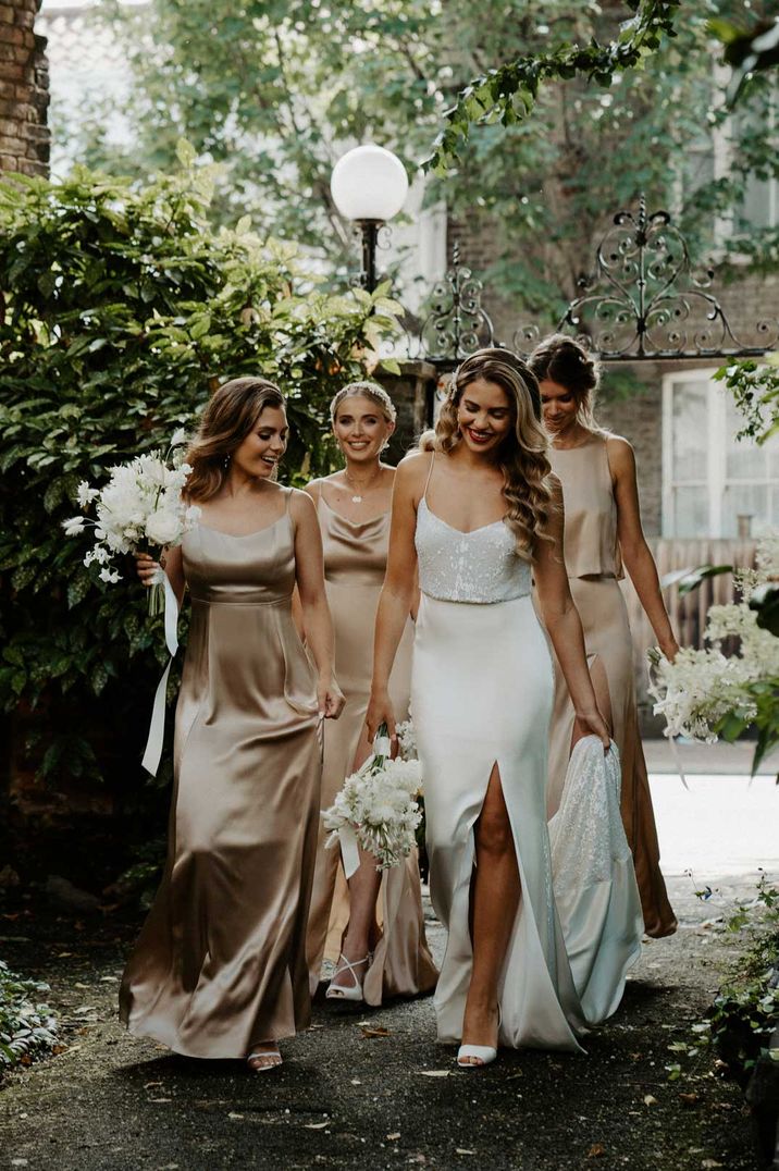 Bride in front slit satin strappy wedding dress walking with bridal party in Constellation Ame sleeveless champagne gold satin bridesmaid dresses 