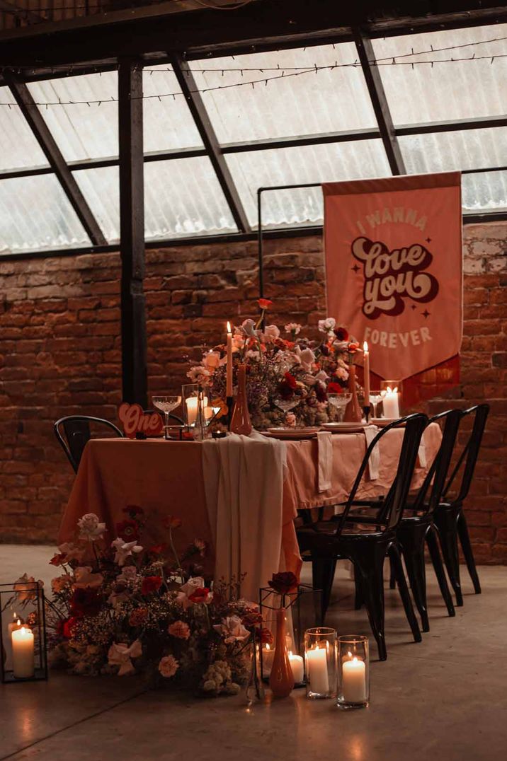 Valentines-inspired wedding tablescape at The Shack Revolution wedding venue with large fabric wedding banner, rose and foliage wedding centrepieces and pillar candles 