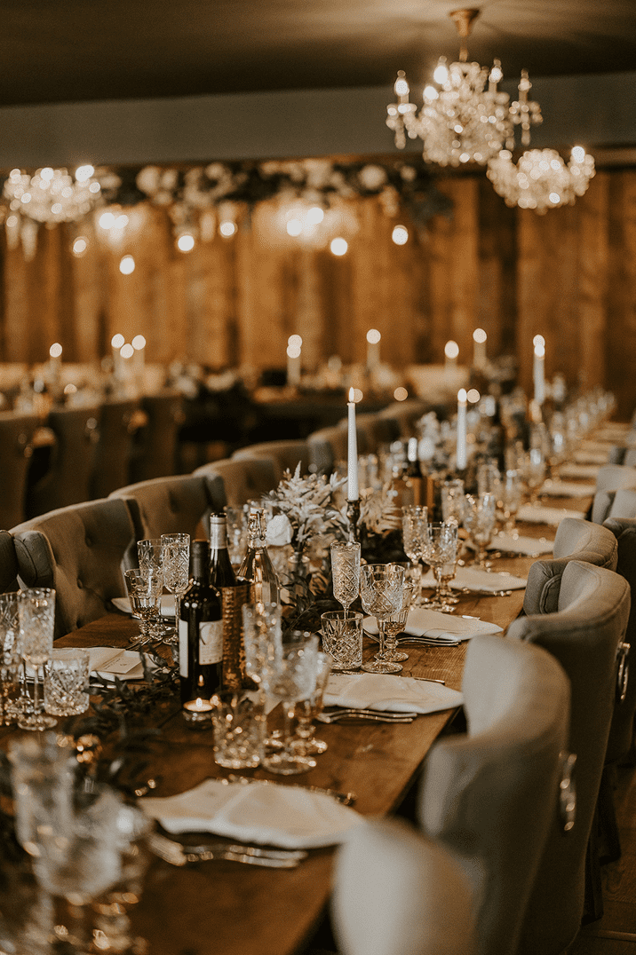 Simple wedding tablescape with greenery, crystal glassware, white taper candles and chandeliers 