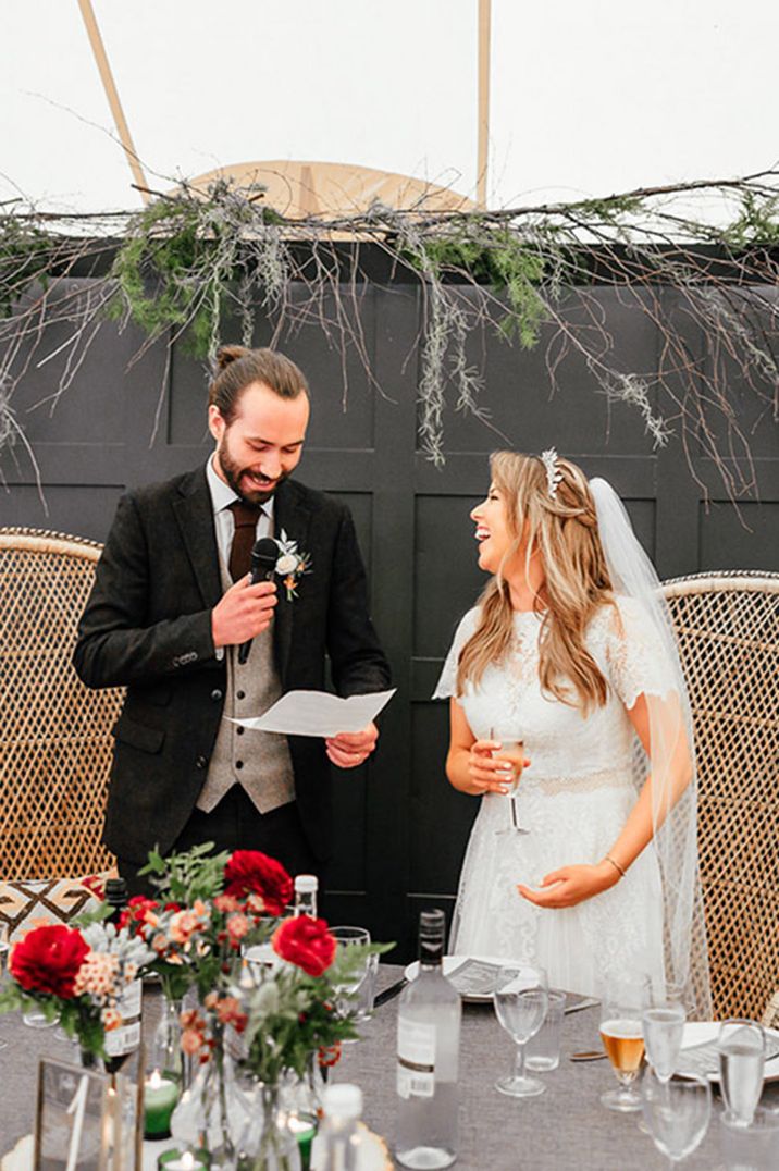 The bride and groom stand in front of the peacock chairs as they read out their wedding speeches 